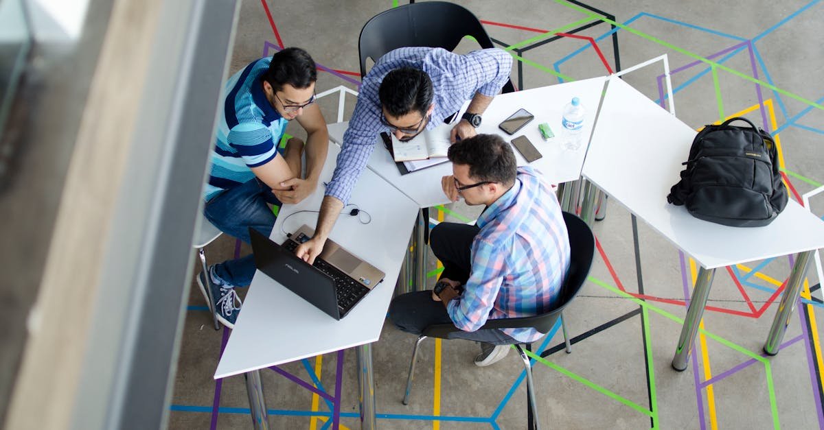 Three men collaborating over a laptop in a modern, geometric-themed office space.